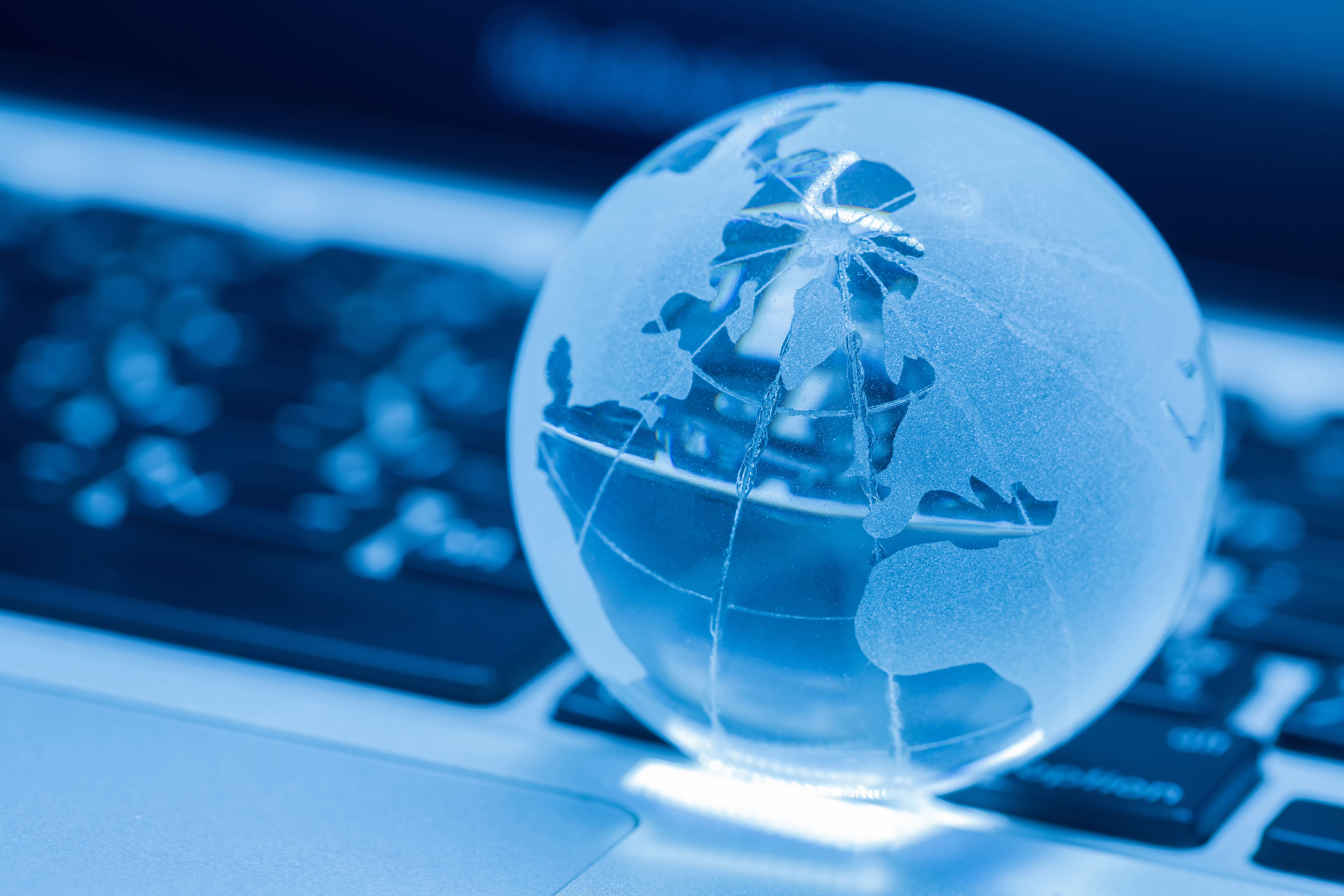 Glass globe on a laptop keyboard, blue light, suggesting global digital reach