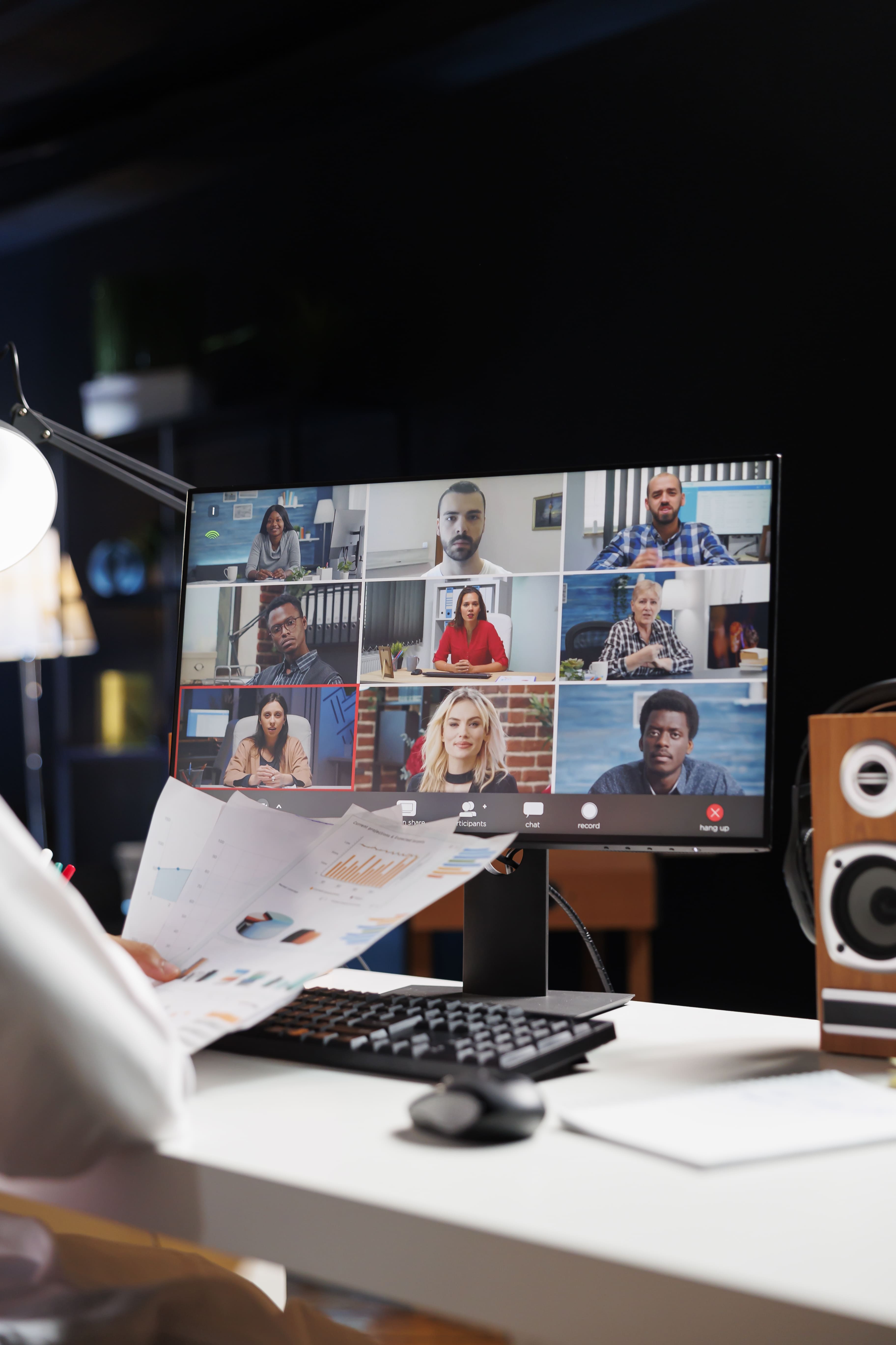 Video conference grid on a monitor during a remote webinar, with printed charts on a desk